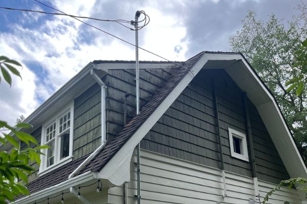 A two-story house with green and white siding, a steep roof, a metal utility pole attached, and a small window on the upper floor.