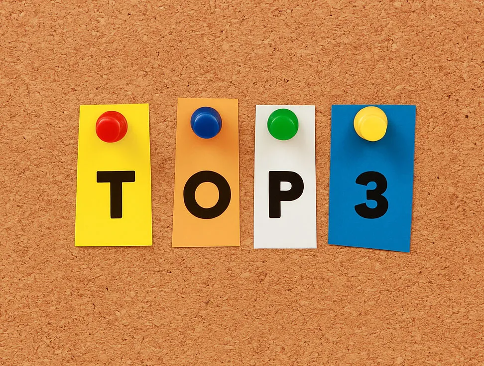 Four colored notes pinned to a corkboard spell out "TOP 3" in bold black letters with colored push pins on each note.